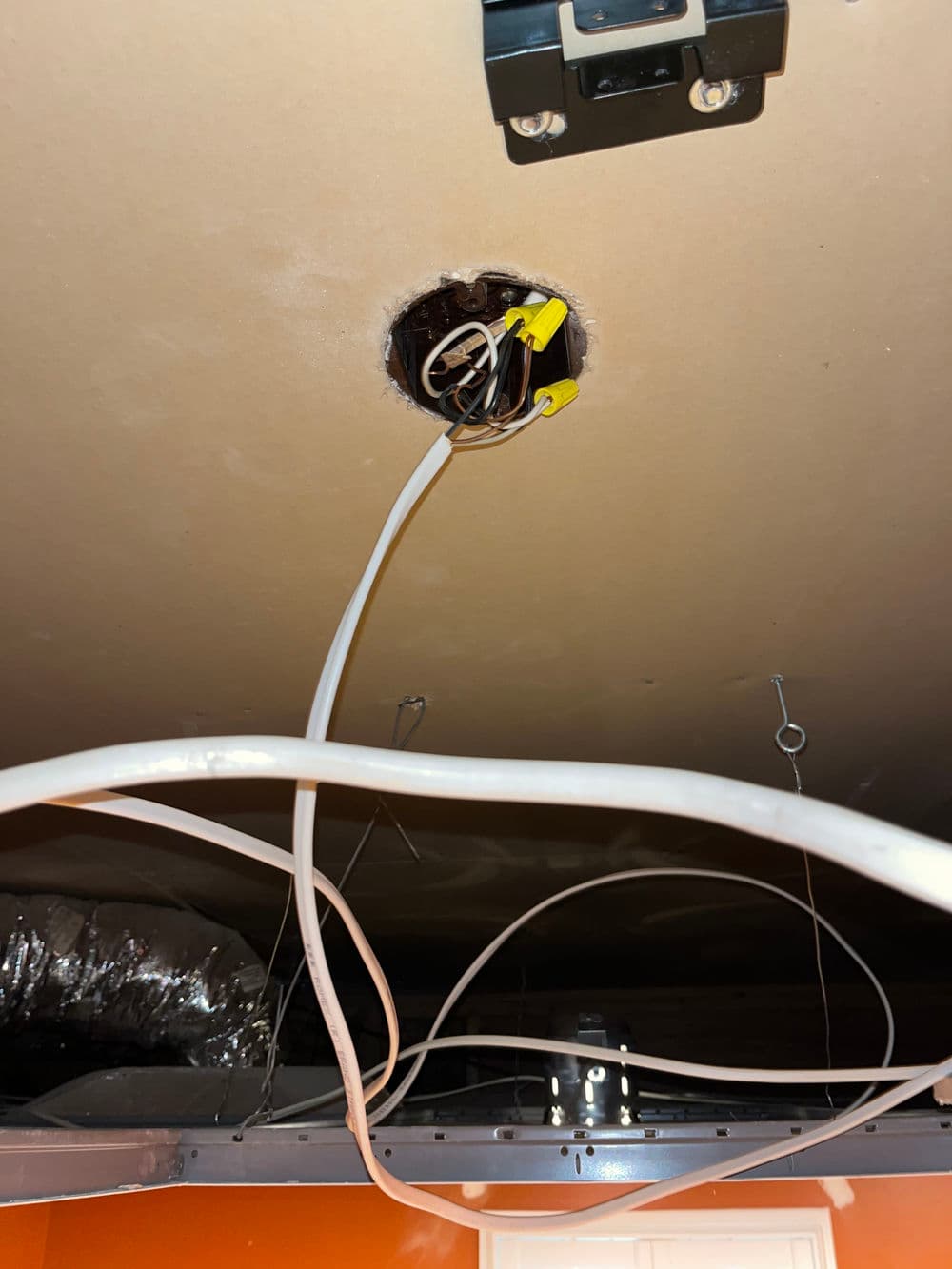 Electrical wires and junction box visible in ceiling hole with insulation in the background.